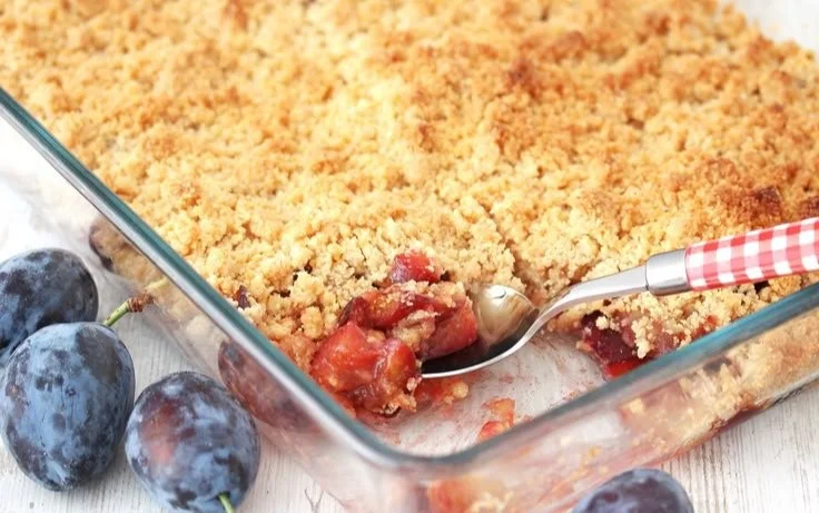Ein köstlicher Zwetschgen Crumble auf einem Teller verziert mit frischen Pflaumen