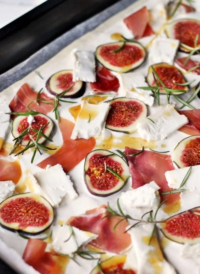 Flammkuchen mit Feigen und Ziegenkäse auf einem Holzbrett serviert.