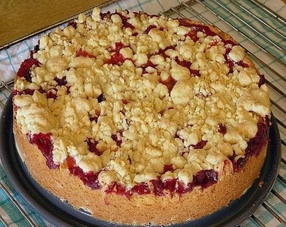 Pflaumenkuchen mit Streuseln auf einem Holzbrett serviert.
