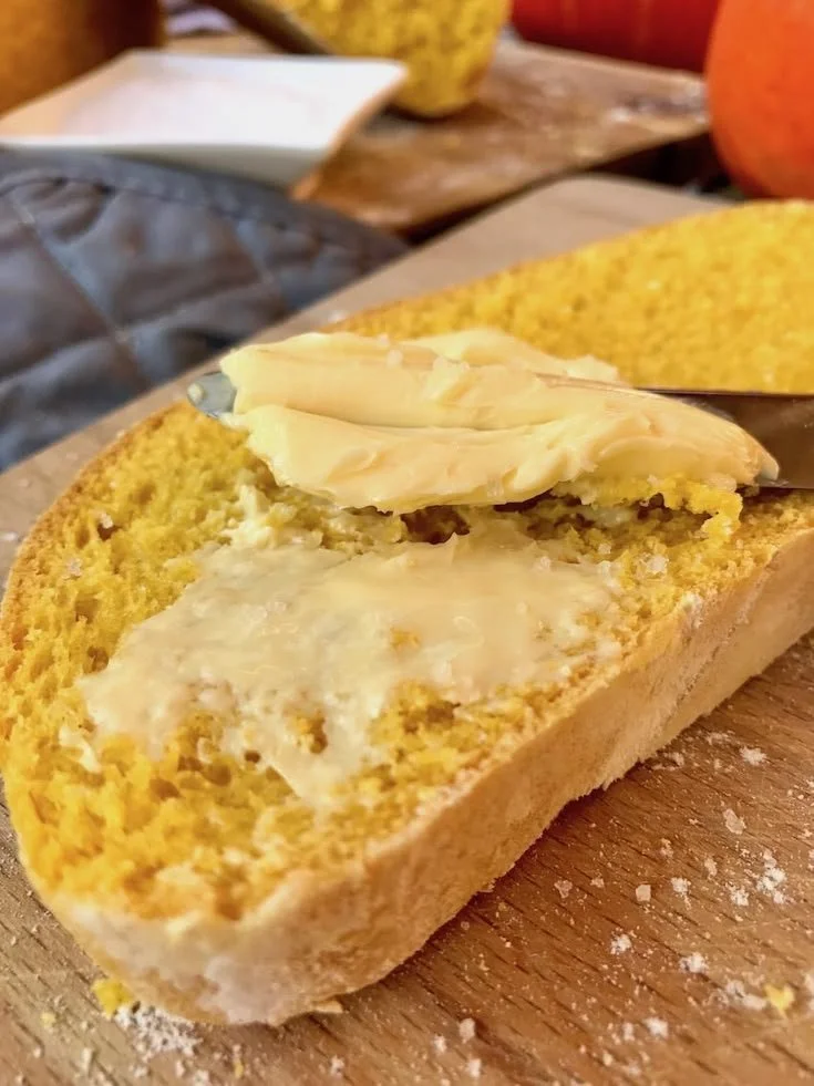 Fluffiges Kürbisbrot auf einem Holzbrett mit Kürbissen im Hintergrund